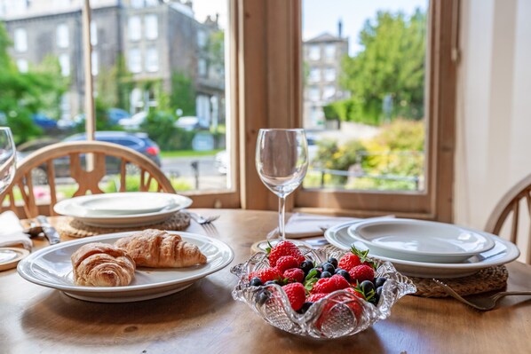Una mesa de desayuno con croissants, un bol de bayas frescas y una copa de vino.
