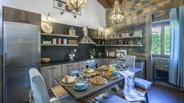 A modern kitchen with a stone wall, wooden shelves, and a dining area with a table set for four. - Dandy Villas Palios Agios Athanasios | Attic | Fireplace | Up to 8 (Agios Athanasios)