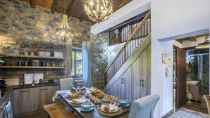 A dining area with a stone wall, wooden beams, and a staircase leading to an upper level. - Dandy Villas Palios Agios Athanasios | Attic | Fireplace | Up to 8 (Agios Athanasios)