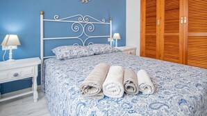 A bedroom with a blue and white patterned bedspread, a white metal headboard, two bedside tables with lamps, and a wooden wardrobe. - Apartamento El rosal de Huertas (Cádiz)