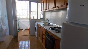 Cucina con mobili in legno, piano cottura a gas, lavello e lavatrice.