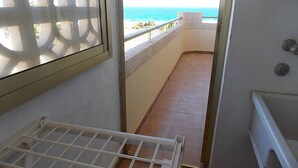 Un balcone con vista sull'oceano, ringhiera in metallo bianco e pavimento piastrellato.