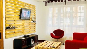 Een woonkamer met een wandmeubel van hout, een rode stoel, een klein rond tafeltje en een houten salontafel met wielen.