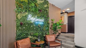 A lobby with a green wall, two brown leather chairs, a small wooden table, and a neon sign that reads "Bay Breeze Pillow Lounge". - Baybreeze Apartments by Lowkl (Miami Beach)