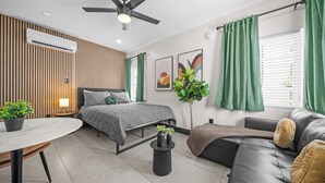 A modern bedroom with a bed, a sofa, a dining table, and a ceiling fan. - Baybreeze Apartments by Lowkl (Miami Beach)