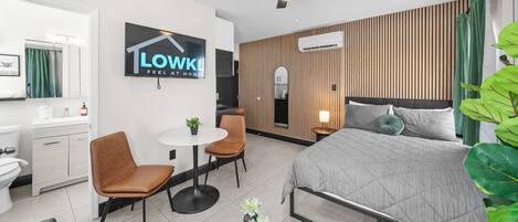 Una habitación de hotel moderna con cama, escritorio, silla, mesita y ventilador de techo.