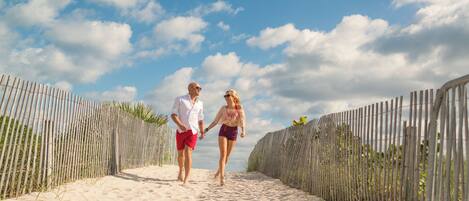 A sandy beach path with a wooden fence on both sides, leading to the sea.