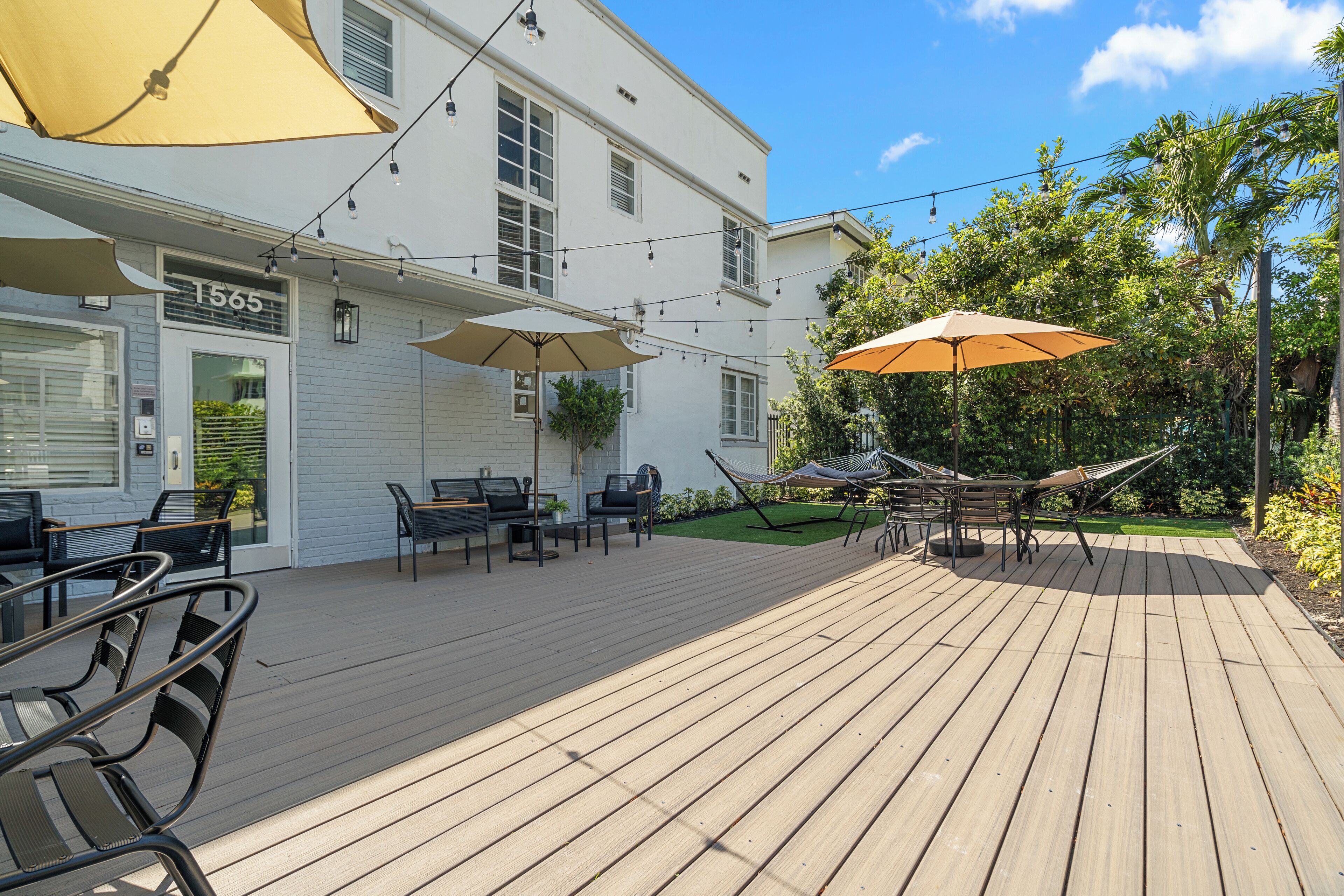 A wooden deck with outdoor seating, umbrellas, and a building with a number sign.