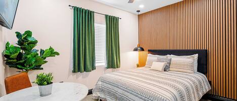A bedroom with a bed, a ceiling fan, a TV, a potted plant, and a dining table.