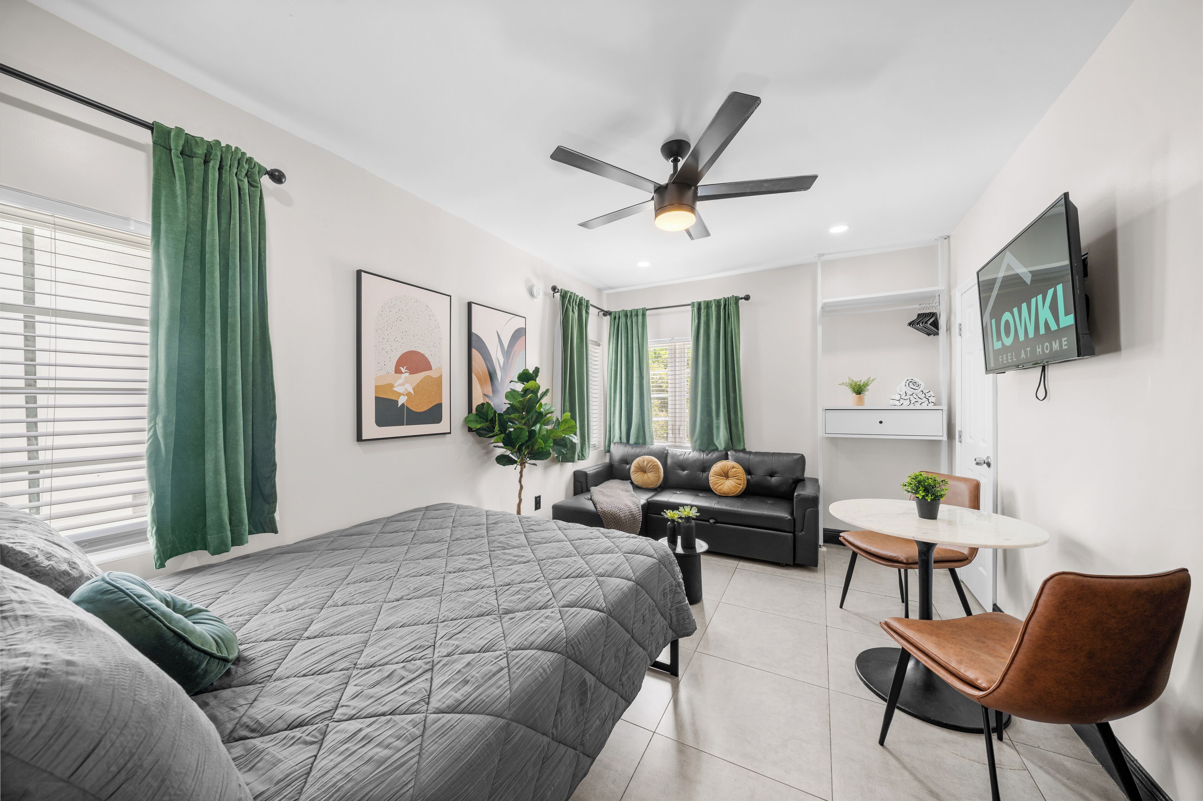 A modern hotel room with a bed, a sofa, a dining table, and a TV.