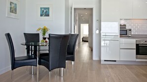 Une cuisine moderne avec des meubles blancs, des appareils en acier inoxydable et un coin repas comprenant une table en verre et des chaises noires.