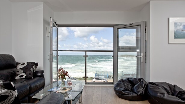 Un salon moderne doté d’une grande porte vitrée donnant sur un balcon avec vue sur l’océan.