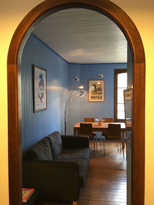 Un interior con un arco de madera que conduce a un comedor con una mesa y sillas, un sofá y carteles enmarcados en las paredes.