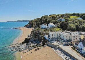 A coastal property with multiple buildings, a beach, and a cliff overlooking the sea.