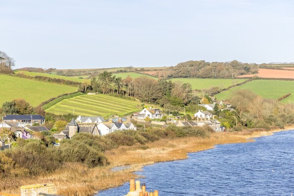 A coastal village with houses along the water, a green field, and a river.