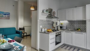 Une cuisine compacte avec des meubles blancs, une cuisinière à gaz, un four à micro-ondes et un évier. On y trouve également un coin repas avec un canapé bleu et une table dressée pour deux personnes.
