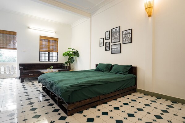 A bedroom with a bed, a bedside table, a potted plant, and a wall with framed pictures.