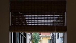 A view through a window with blinds, revealing a narrow street with buildings on either side. - Michi House (Hanoi)
