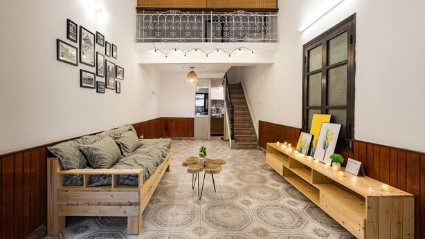 A cozy room with a loft area, a staircase, and a long wooden bench with artwork. - Michi House (Hanoi)