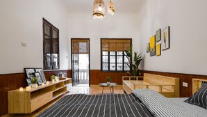 A bedroom with a large bed, wooden headboard, bedside tables, a wooden bench, and a small table with a plant. - Michi House (Hanoi)