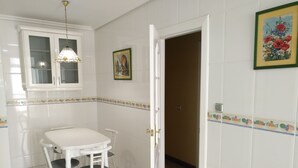 Comedor con mesa y sillas blancas, lámpara colgante y puerta que da a otra habitación.