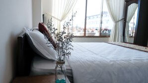 A bedroom with a bed, a nightstand, a vase with dried flowers, and a window with curtains. - Bukchon Da Lat Hotel (Xuan Huong - Da Lat)
