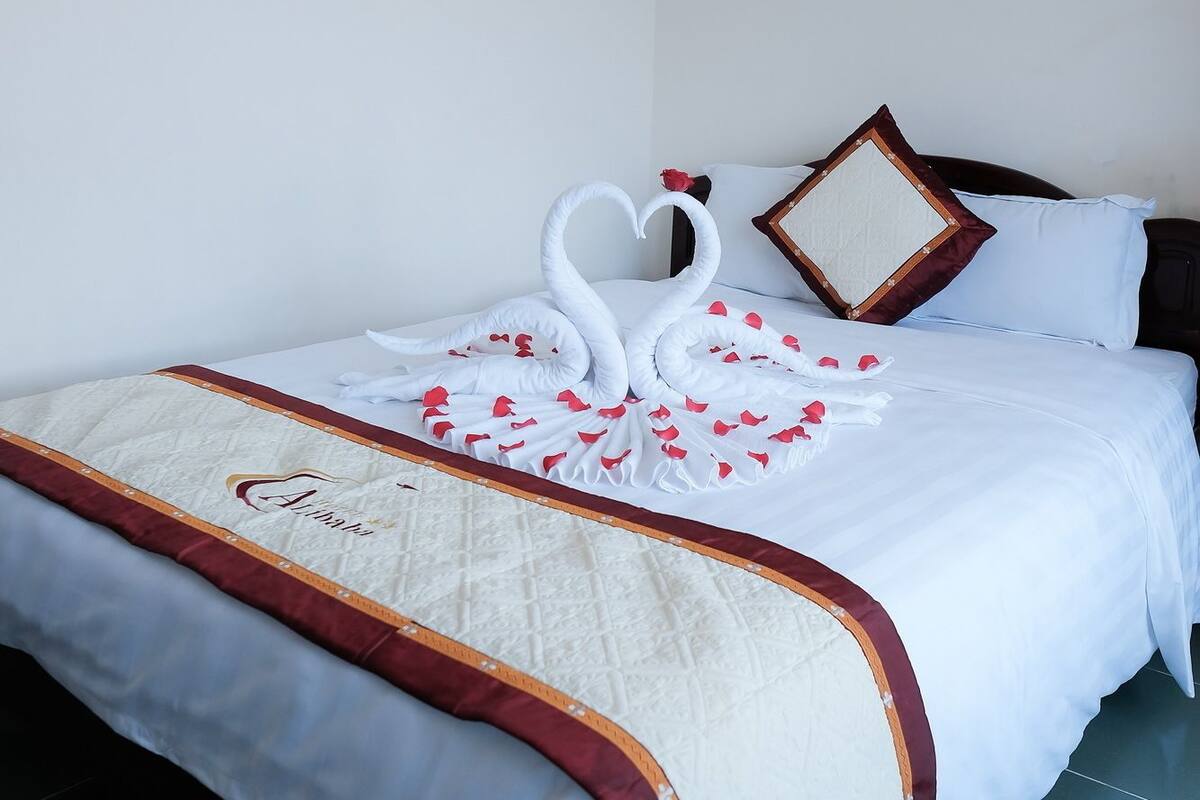 A neatly made bed with a white bedspread, a decorative heart-shaped pillow, and a swan-shaped pillow.
