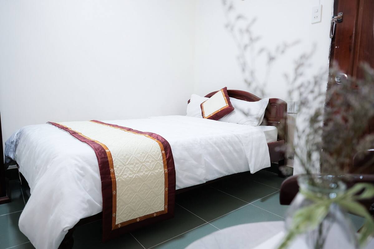 A single bed with a white and maroon bedspread, a wooden headboard, and a white pillow.