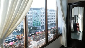 A room with a large window overlooking a cityscape, a potted plant on the windowsill, and a dark wooden cabinet. - Bukchon Da Lat Hotel (Xuan Huong - Da Lat)