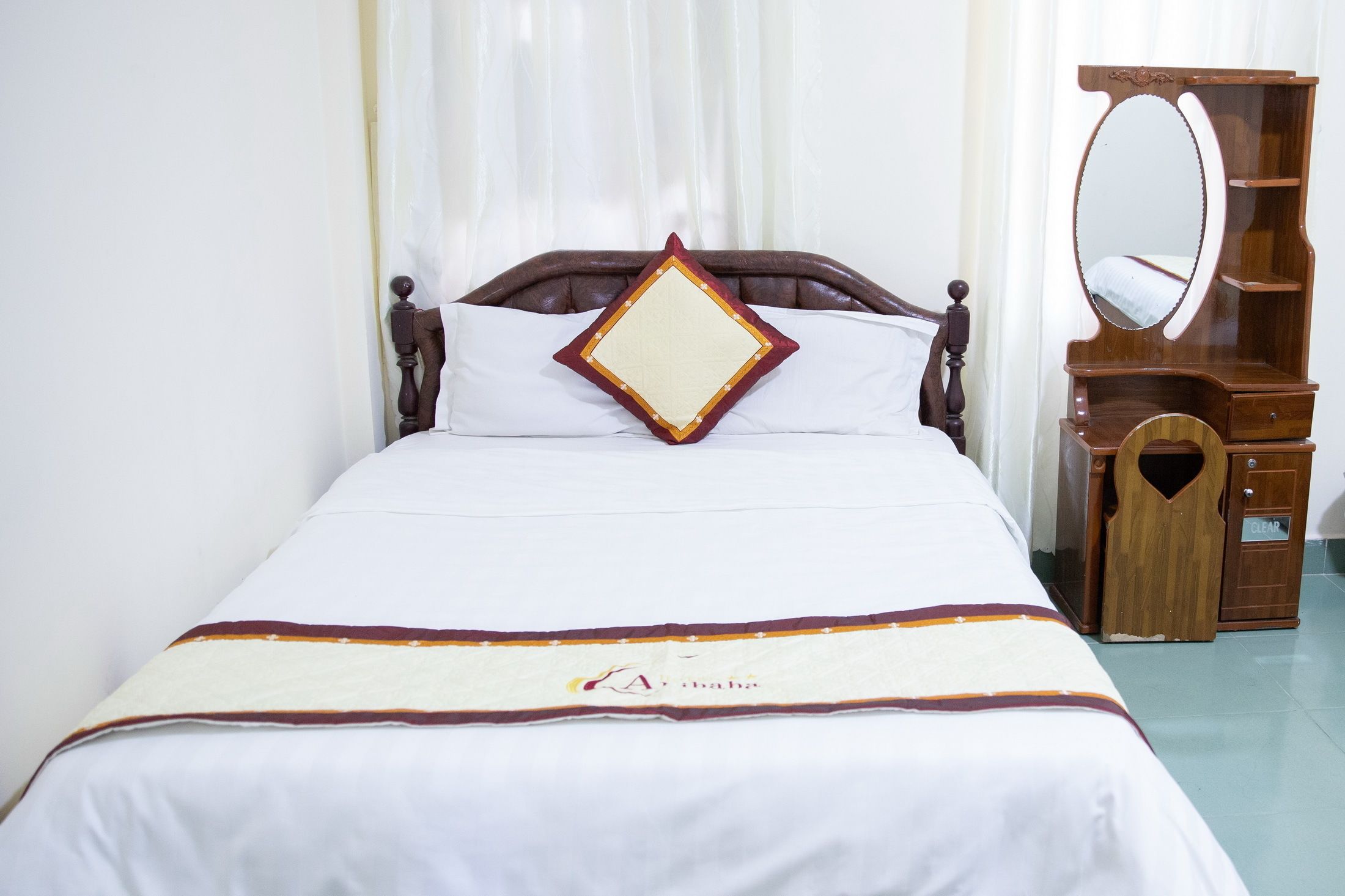 A neatly made bed with a diamond-shaped pillow and a bedspread with a logo.