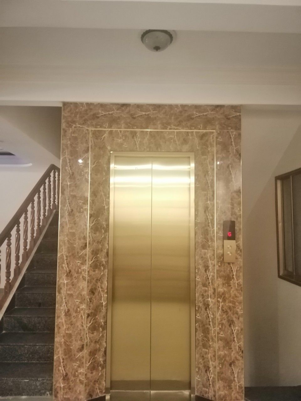 Un ascensor con pared de mármol, una escalera y un panel de control adosado a la pared.