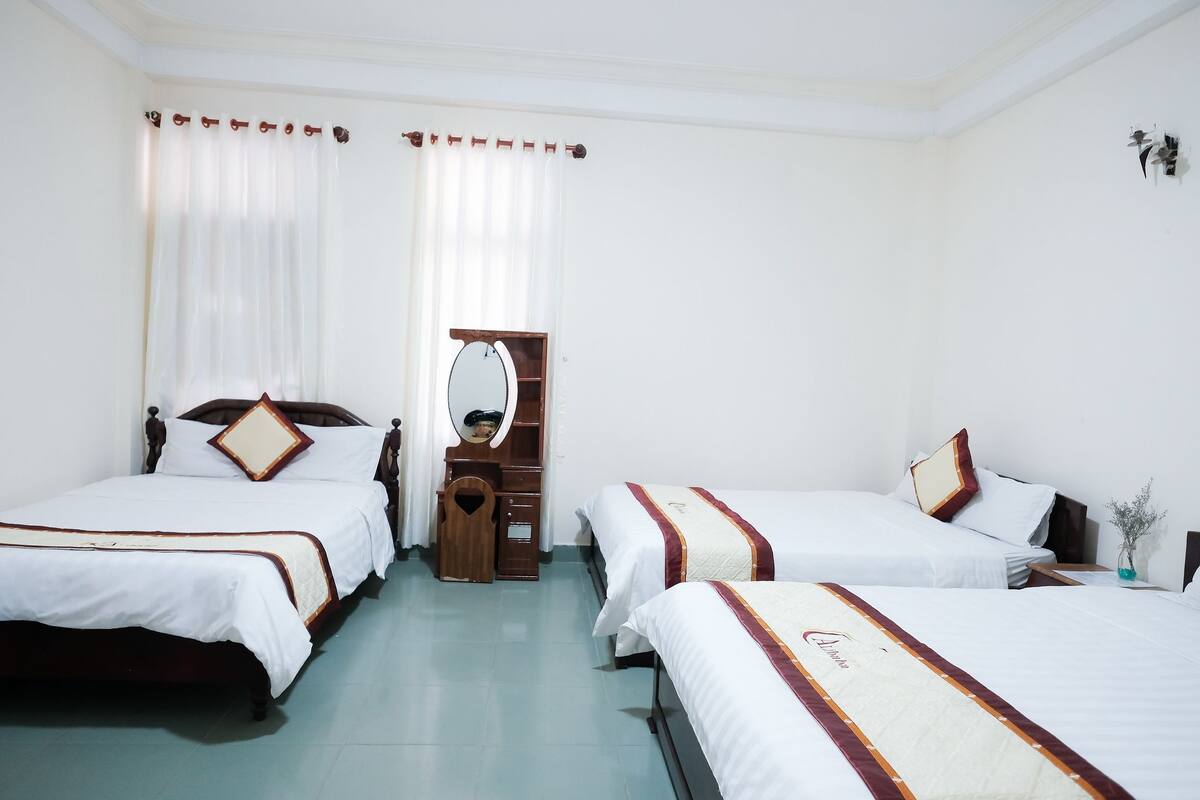 A hotel room with two single beds, a wooden dresser, a mirror, and a small table with a vase.