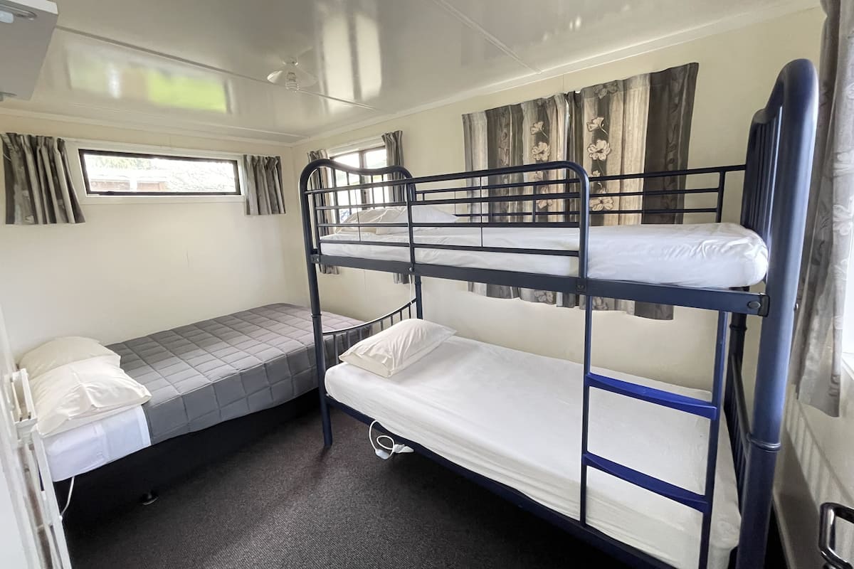 A bunk bed room with a window, curtains, and a ceiling fan.