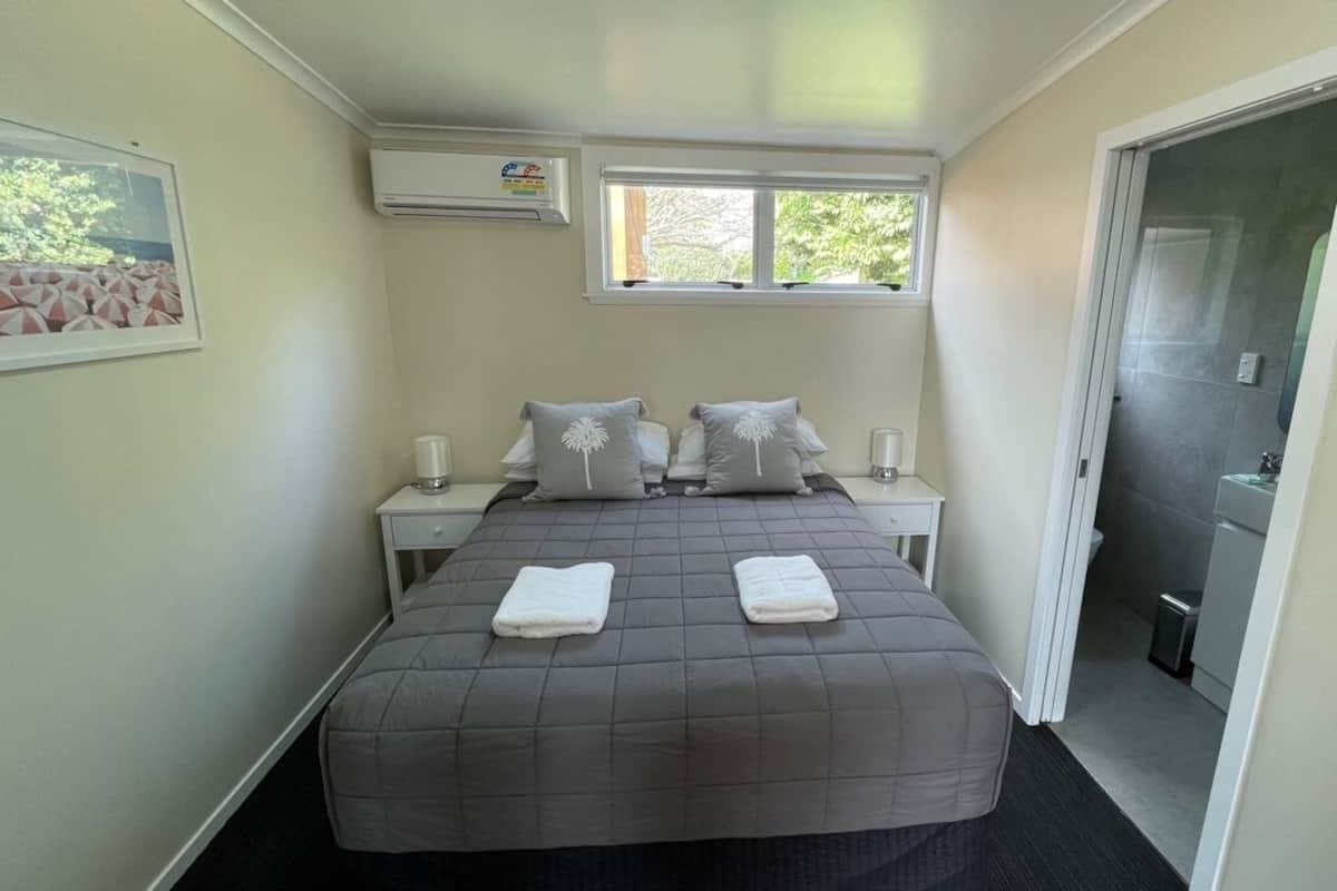 A bedroom with a bed, two bedside tables, a window, and a door leading to a bathroom.