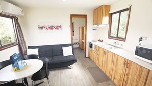 A compact kitchen with wooden cabinets, a white countertop, and a built-in microwave. There's a small dining area with a table and chairs. - Orere Point TOP 10 Holiday Park (Orere Point)