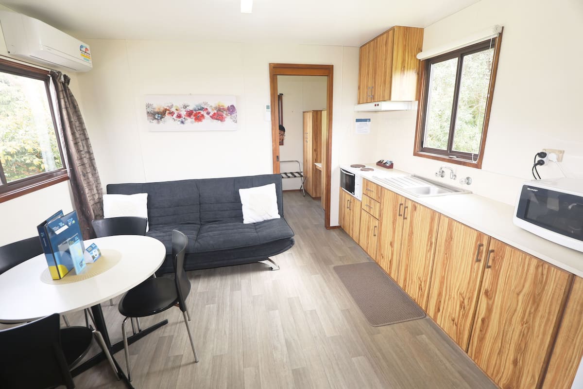 A compact kitchen with wooden cabinets, a white countertop, and a built-in microwave. There's a small dining area with a table and chairs.