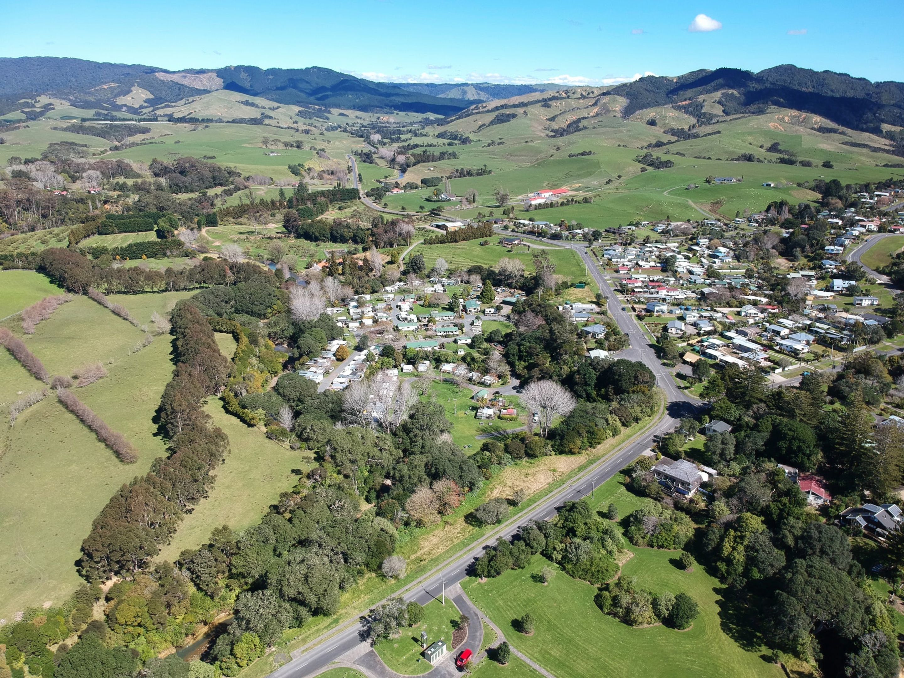 An aerial view of a rural area with a small settlement, roads, and green fields.