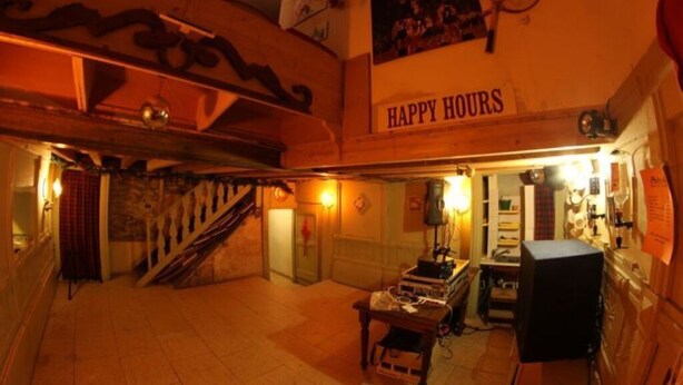Tunnelmallinen huone, jossa on portaikko, pöytä, jossa on esineitä, ja kyltti, jossa lukee ”Happy Hours”.