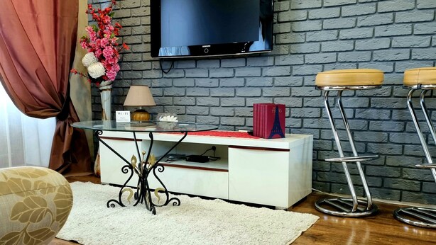 Ein Wohnzimmer mit Backsteinwand, Flachbildfernseher, weißem Schrank, Couchtisch, Sofa und zwei Barhocker.