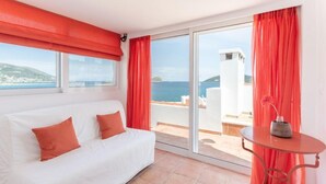 A room with a white sofa, red curtains, a small table with a vase, and a view of the sea. - Baywatch Appartment close to the Airport at Porto Rafti 30 meters from the sea (Porto Rafti)