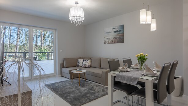 A modern living room with a sofa, dining table, chandelier, and a painting on the wall.