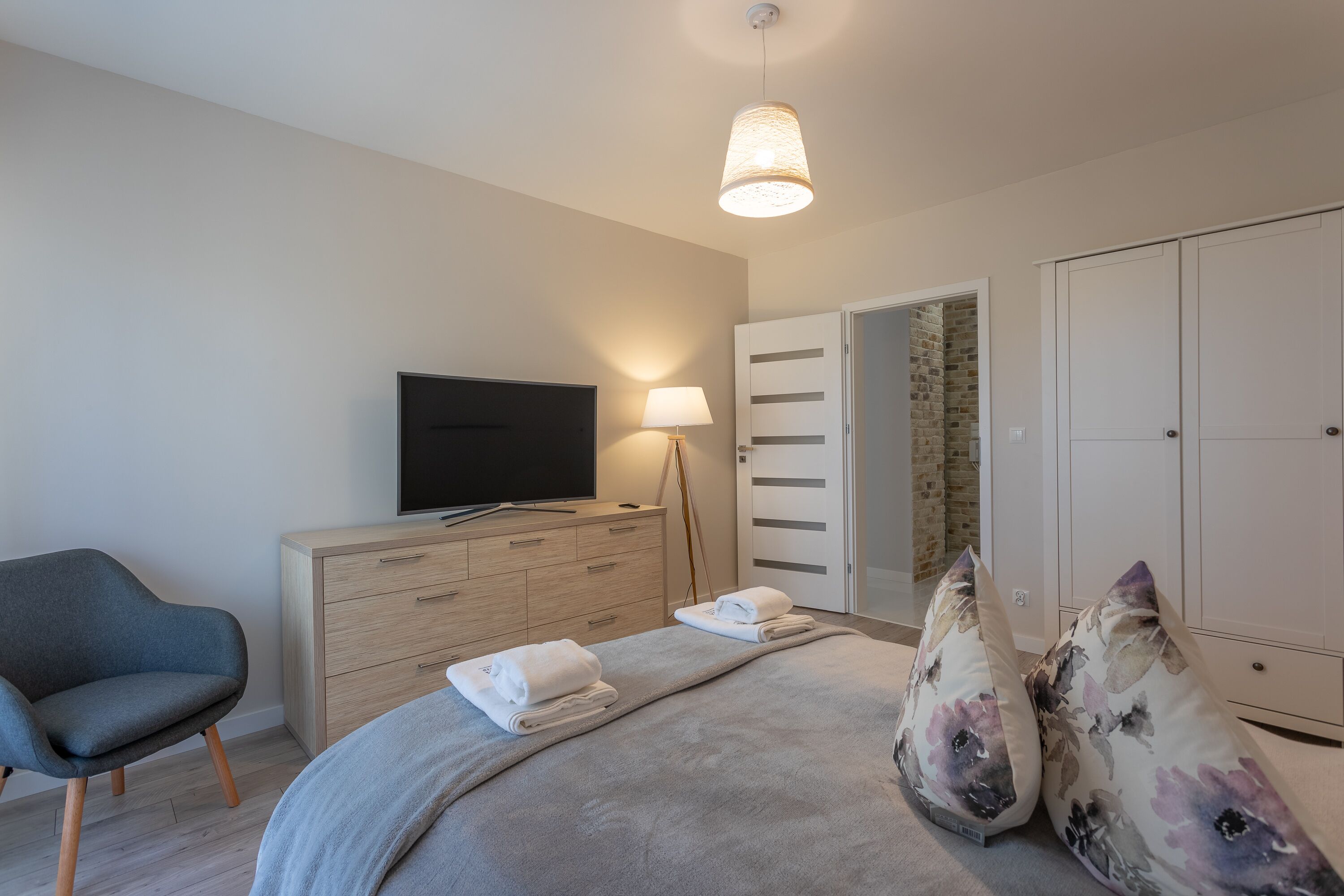 A bedroom with a bed, a TV, a dresser, a chair, and a wardrobe.