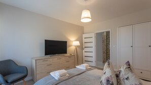 A bedroom with a bed, a TV, a dresser, a chair, and a wardrobe.