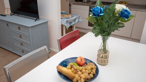 A dining area with a table set for two, a vase with flowers, and a plate with fruits and grapes. - 65 sqm apartment 50 meters from the sea (Albissola Marina)
