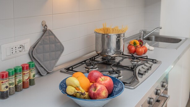 A kitchen with a stove, a pot of spaghetti, a bowl of fruit, and various spices. - 65 sqm apartment 50 meters from the sea (Albissola Marina)
