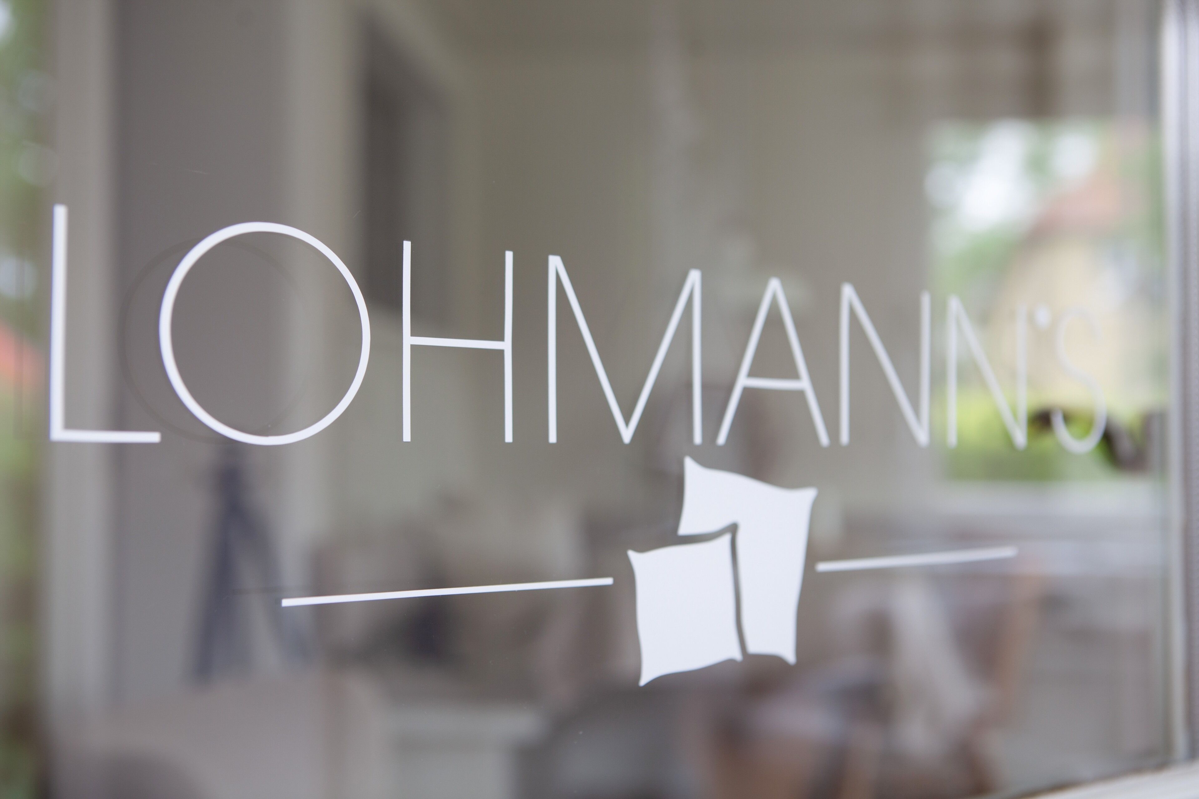 Ein Glasfenster mit dem Schriftzug "LOHMANN'S" und einer stilisierten Gebäudedarstellung.