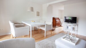 A modern living room with a white sofa, a dining table with chairs, a TV on a stand, and a wooden cabinet. - Lohmann's apartment (Garstedt)