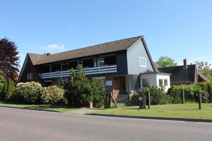 Une maison à deux étages avec un balcon, une véranda à l’avant et un petit garage attenant.