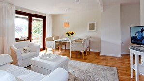 A modern living room with a white sofa, a dining table with chairs, a TV, and a window with curtains. - Lohmann's apartment (Garstedt)