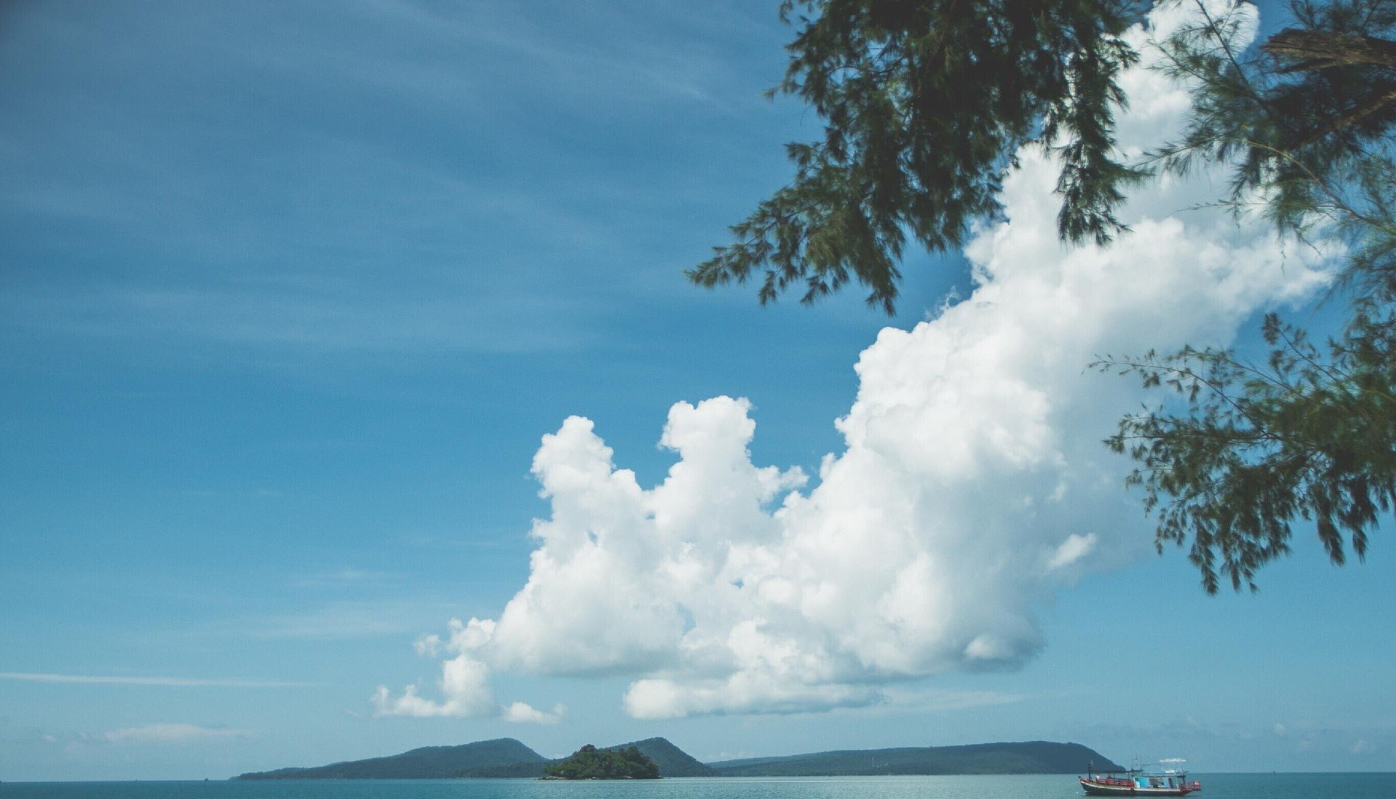 A coastal landscape with a boat on the water, a clear sky, and a distant island.